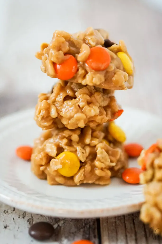 A stack of 3 no bake rice krispies cookies with reeses pieces on a white plate. 
