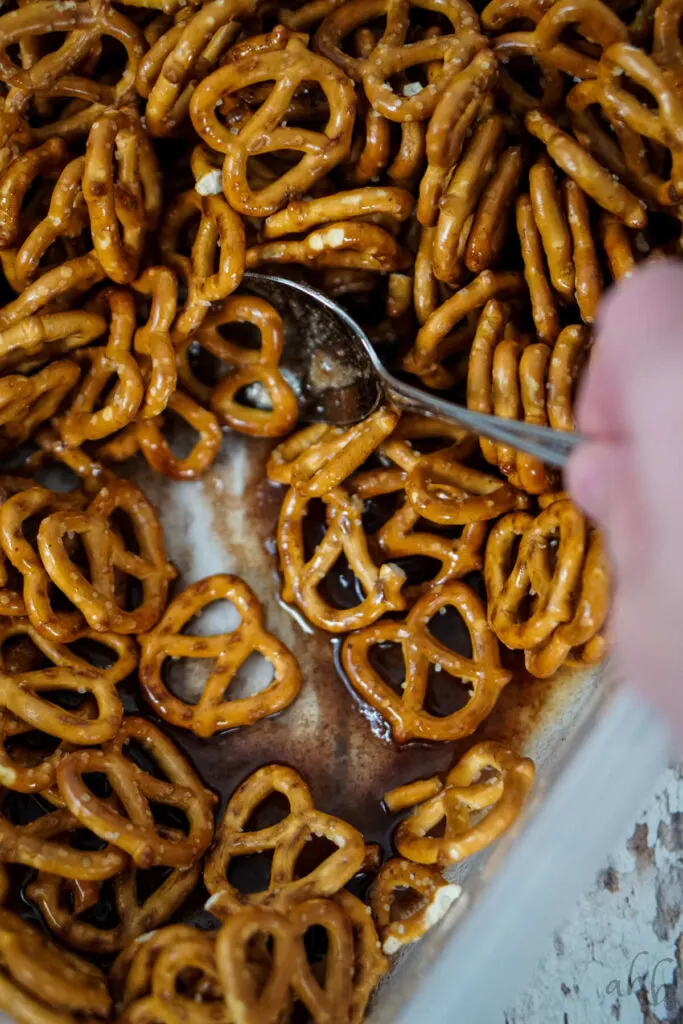Pretzels are mixed into the melted butter, sugar, corn syrup, and cinnamon with a spoon.