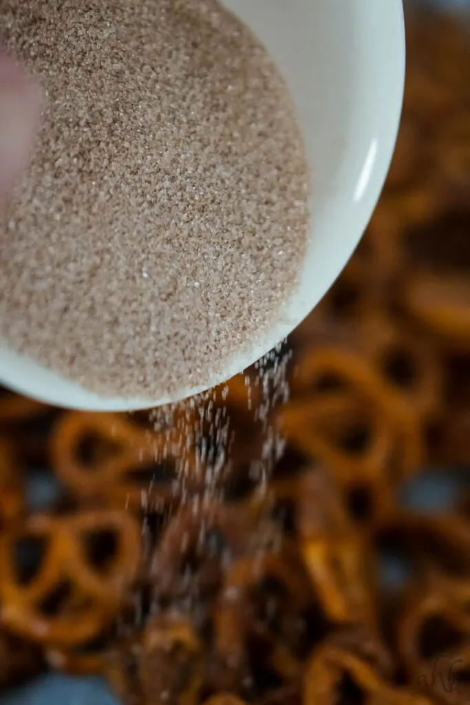A white bowl of cinnamon sugar is sprinkled onto the coated pretzels.