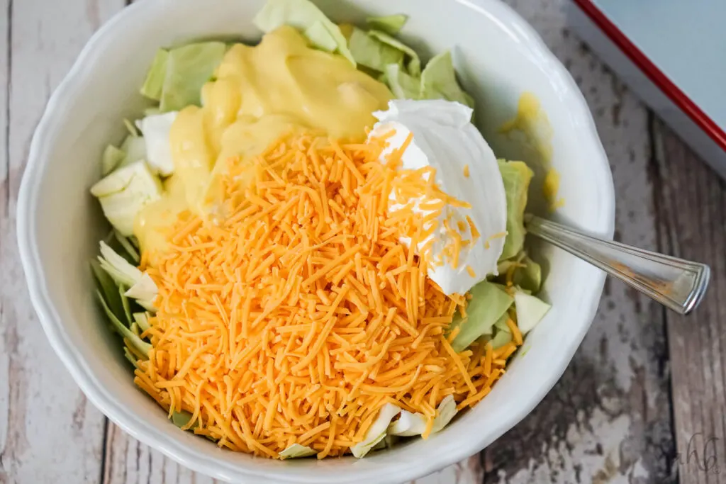 The cabbage, shredded cheese, cream of chicken soup, and sour cream are added to the bowl and stirred together.