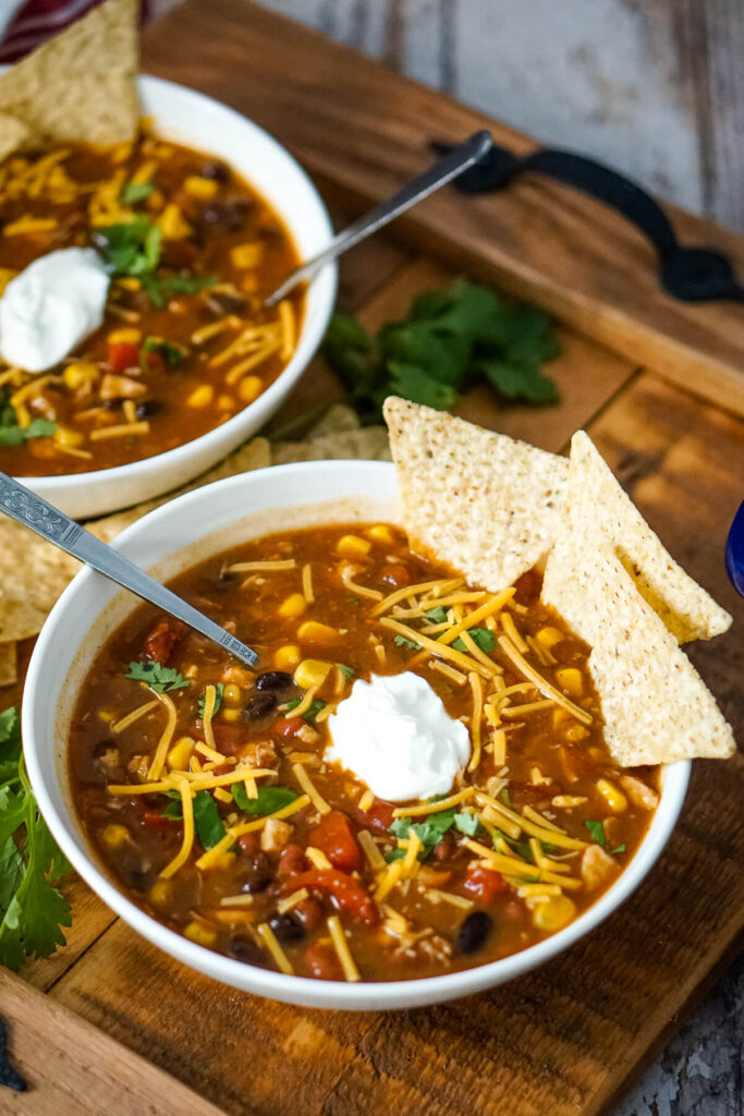 A bowl of 7 Can Chicken Taco Soup served with shredded cheddar cheese, sour cream, cilantro, and tortilla chips. 