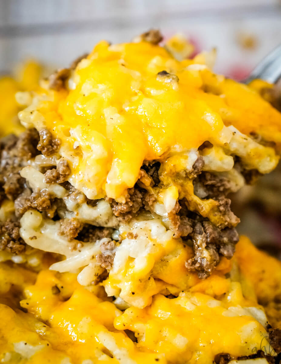 A scoop of cheesy Hamburger Hashbrown Casserole is lifted out of the  pan.