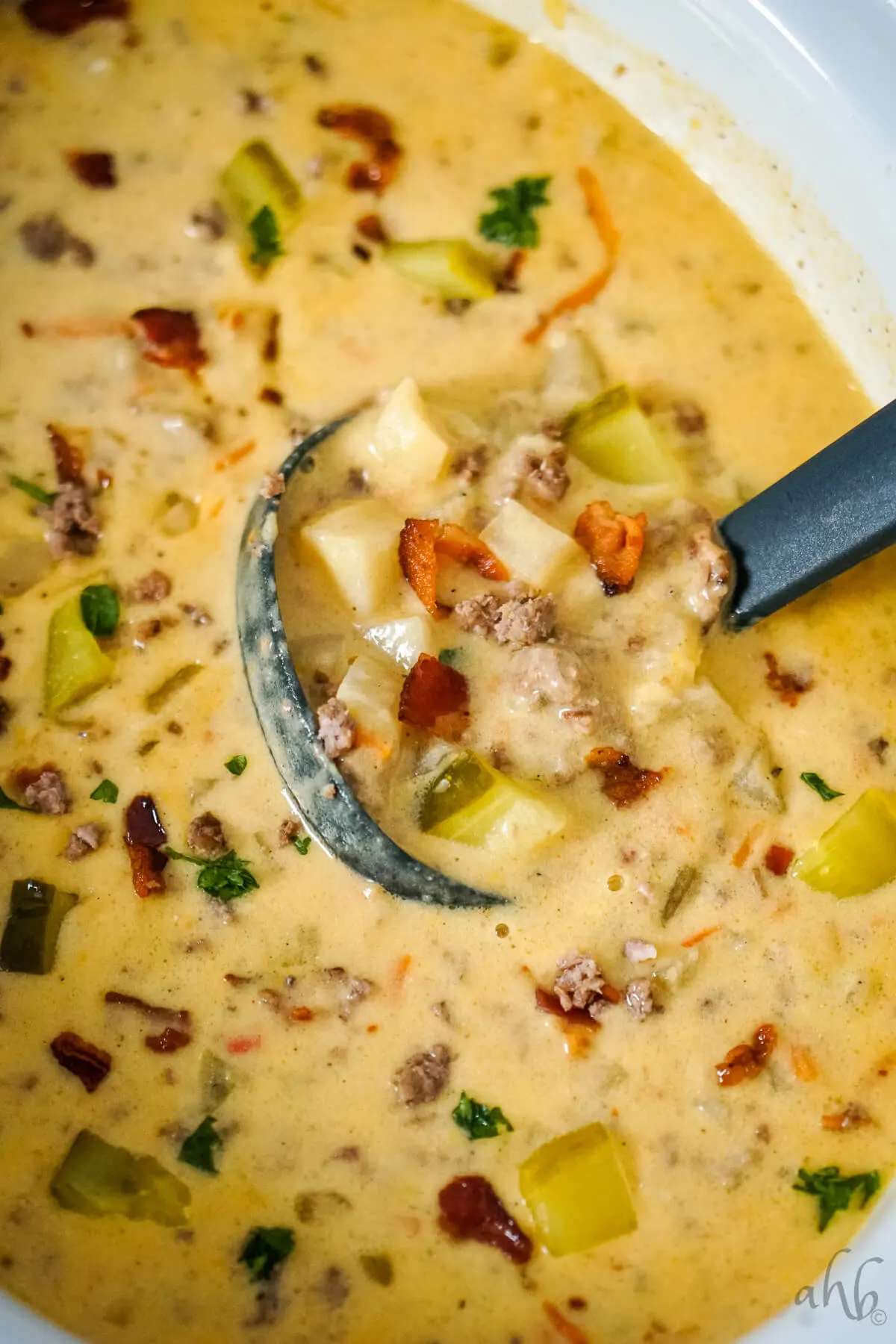 A ladle stirring Bacon Cheeseburger Soup in the slow cooker.