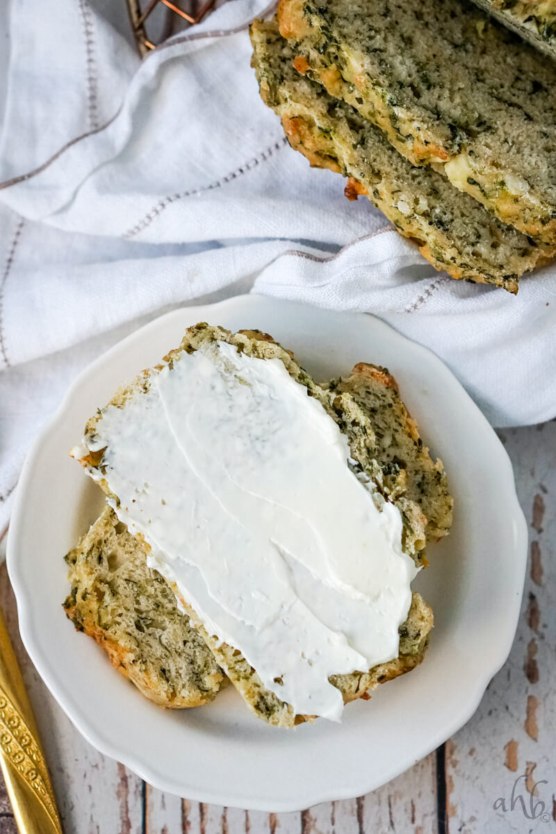 Two slices of Spinach Feta Beer Bread served with a spread of cream cheese on a white plate.