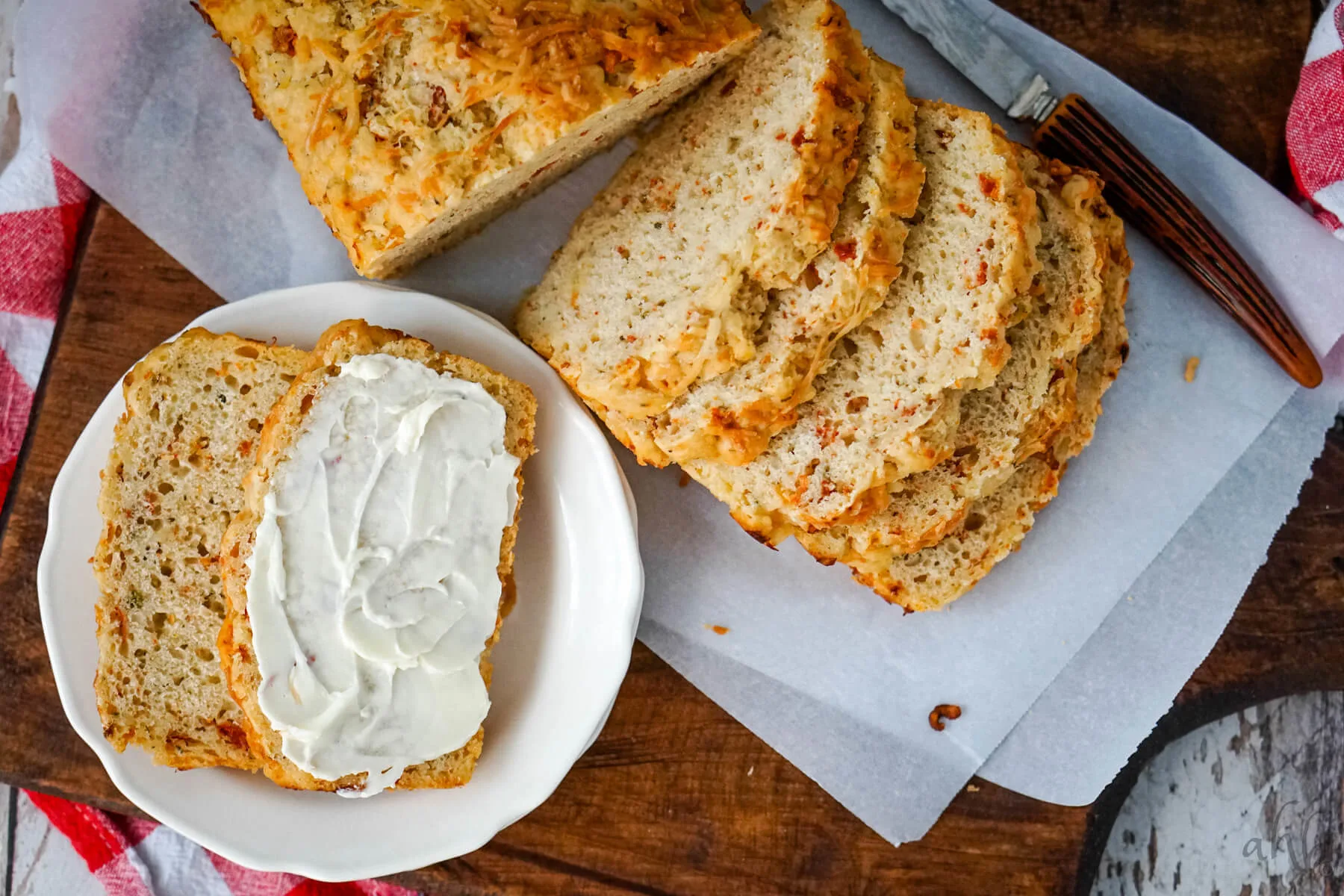 A sliced loaf of Sun Dried Tomato and Parmesan Beer Bread and two slices served on a white plate with cream cheese. 