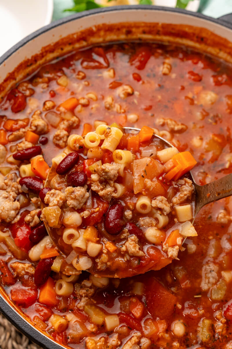 A ladle holds a scoop of Pasta Fagioli over the pot.