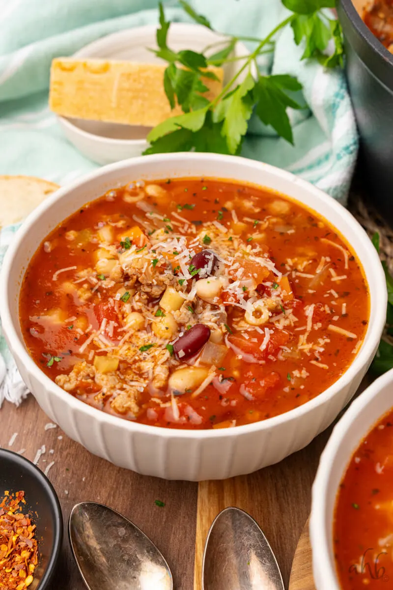 A bowl of Easy Pasta Fagioli soup is served in a white bowl and topped with shredded Parmesan cheese.