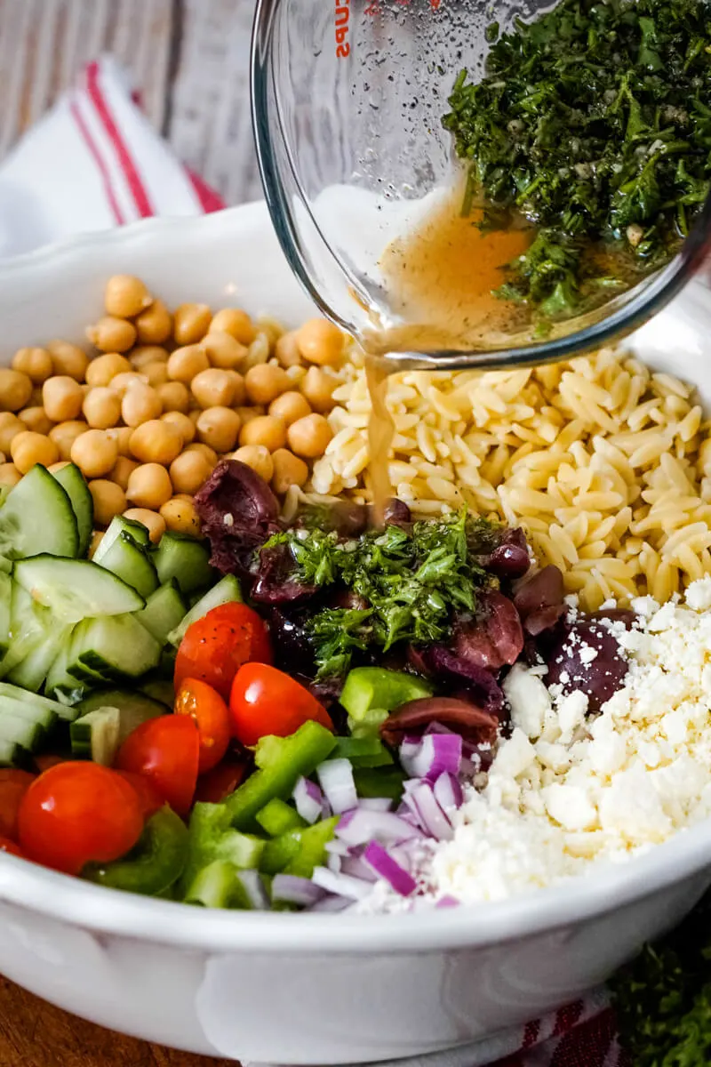 All the ingredients of the salad are added to a large white bowl while the homemade dressing is poured over them.
