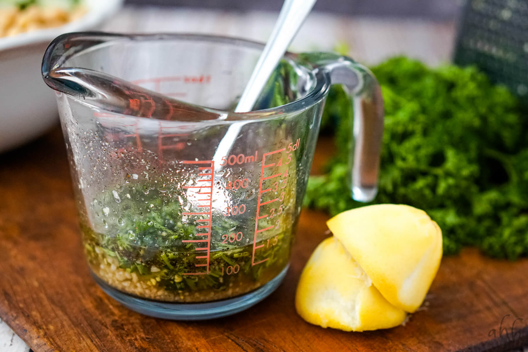 A glass measuring cup is filled with the ingredients for the salad dressing and is stirred with a fork.