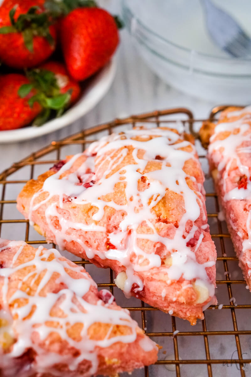 A close up image of a strawberry cake mix scone on a wire rack with fresh strawberries in the background. 