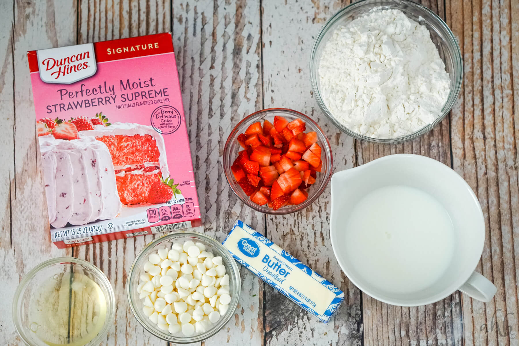 The ingredients needed to make strawberry cake mix scones: strawberry cake mix, chopped strawberries, flour, egg white, white chocolate chips, butter, and milk. 