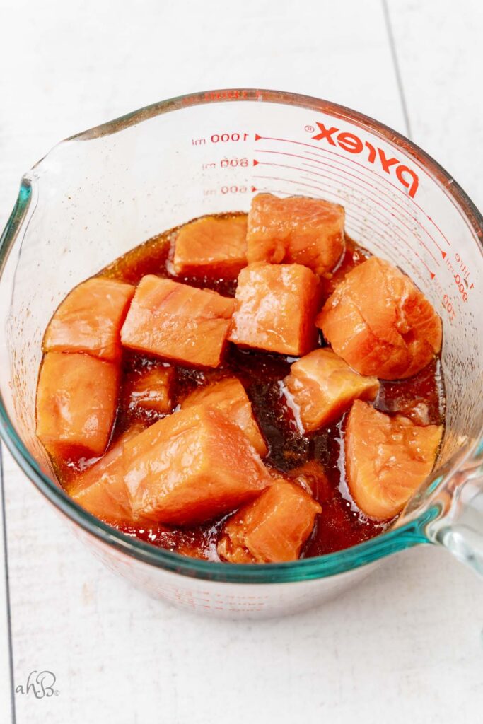 The cubed salmon bites are marinated in the mixture in a measuring bowl.